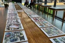 In einem lichtdurchfluteten Ausstellungsraum liegen Comics übersichtlich angeordnet auf einem langen Tisch. Im Hintergrund sitzen zwei Personen und betrachten Comics.