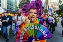 Claude hat geantwortet: Protestfoto von einer Pride-Demonstration in Brasilien (Foto: Mídia Ninja).Protestfoto von einer Pride-Demonstration in Brasilien. Im Vordergrund eine Drag-Person mit pinker Glitzerperücke, dramatischem Make-up und buntem Outfit, die einen Regenbogenfächer mit der Aufschrift „FORA BOLSONARO" hält und die Zunge herausstreckt. Im Hintergrund Demonstrierende mit Regenbogenfahnen und Pride-T-Shirts sowie Polizeibeamt*innen.