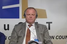 Claude hat geantwortet: Konferenzfoto von Henk Jan van Schothorst, der mit Simultandolmetsch-Kopfhörer und Akkreditierungsausweis sitzt.Konferenzfoto von Henk Jan van Schothorst, der mit Simultandolmetsch-Kopfhörer und Akkreditierungsausweis sitzt. Er trägt einen grauen Anzug mit orangefarbener Krawatte. Im Hintergrund ein Banner mit dem teilweise sichtbaren Schriftzug