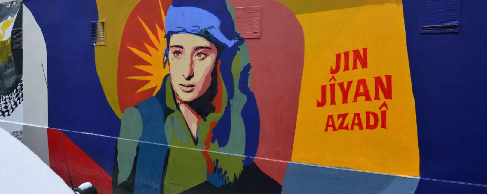 Jin Jiyan Azadi: kurdisch für Women, Life, Freedom / Frauen, Leben, Freiheit. Wandmalerei der Improper Walls in der Schwendergasse in Rudolfsheim-Fünfhaus, Wien. Kurdische Frauenkombatantin von der Künstlerin Btoy nach einem Foto von Maryam Ashrafi