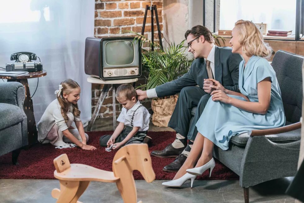 glückliche Eltern sitzen auf dem Sofa und schauen sich kleine Kinder an, die zu Hause mit Dominosteinen spielen, Stil der 50er Jahre glückliche Eltern sitzen auf dem Sofa und schauen sich kleine Kinder an, die zu Hause mit Dominosteinen spielen, Stil der 50er Jahre