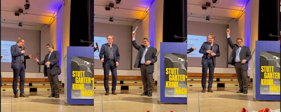 Zwei Männer auf einer Bühne, der eine Mann überreicht dem anderen Mann den Politikkrimipreis 2022 der Heinrich Böll Stiftung Baden-Württemberg im Rahmen der Stuttgarter Kriminächte