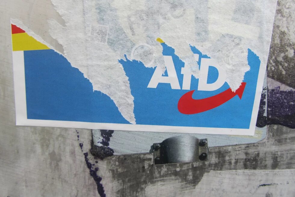 Zerrissenes Plakat der Partei AfD auf metallischem Untergrund, wobei große Teile der oberen Papierschicht entfernt wurden. Nur der blaue Hintergrund, Teile des Parteinamens und der rote Pfeil sind noch erkennbar.