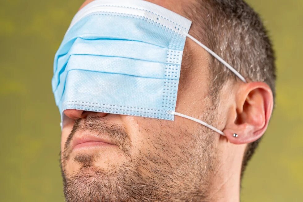 Mann mit medizinischer Gesichtsmaske, die ihm nicht über Mund und Nase, sondern über die Augen gezogen ist