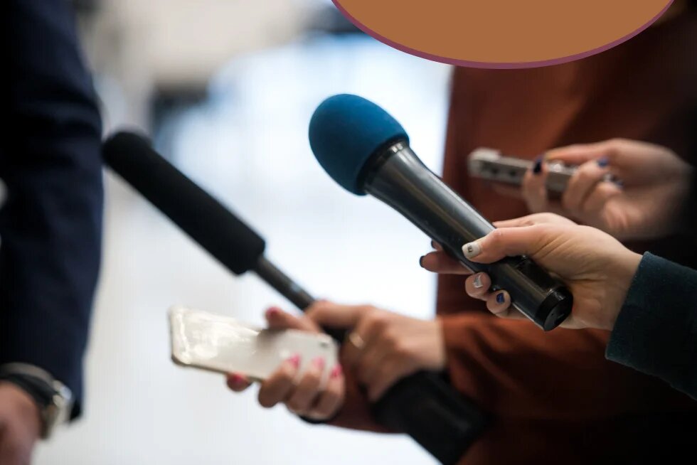 Mehrere Mikrofone werden Personen im Anschnitt entgegengehalten, eine Hand hält zusätzlich ein Smartphone zur Aufnahme. Rechts oben ragt ein oranger Kreis mit violettem Rand ins Bild, im Hintergrund unscharfe Personen in Anzug und rostroter Kleidung.
