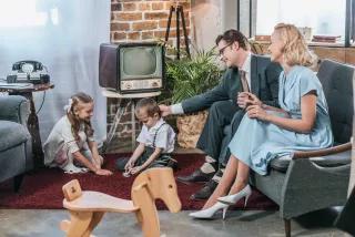 glückliche Eltern sitzen auf dem Sofa und schauen sich kleine Kinder an, die zu Hause mit Dominosteinen spielen, Stil der 50er Jahre glückliche Eltern sitzen auf dem Sofa und schauen sich kleine Kinder an, die zu Hause mit Dominosteinen spielen, Stil der 50er Jahre